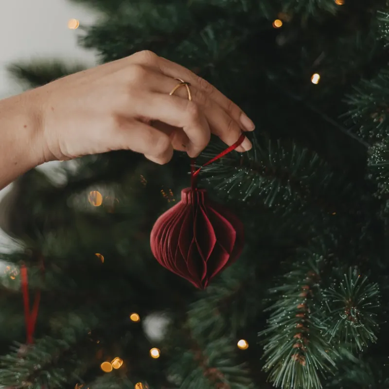 Roter Papieranhänger in Kugelform wird am Weihnachtsbaum aufgehängt